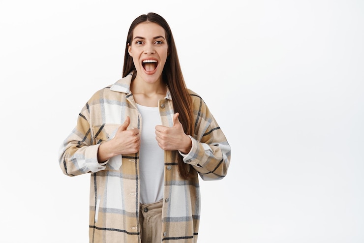 Foto gratuito wow, è stato fantastico la giovane donna eccitata e impressionata mostra i pollici in su e sorride stupita controllando qualcosa di interessante dare una risposta positiva lodi buono eccellente evento sfondo bianco