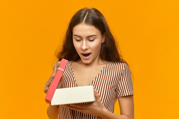 Wow. Studio shot di stupito emotivo giovane femmina europea scatola di apertura con regalo