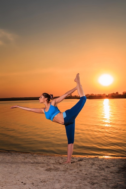yoga al tramonto sulla spiaggia. donna che fa yoga, esegue asana e si gode la vita sul fiume