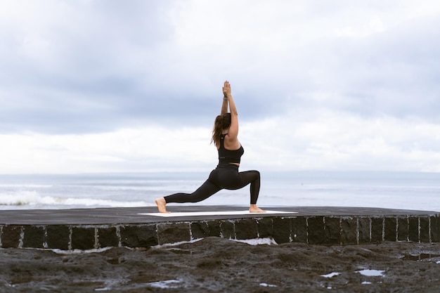 Yoga di pratica della giovane donna su una bella spiaggia all'alba. Cielo blu, oceano, onde, vicinanza alla natura, unità con la natura.