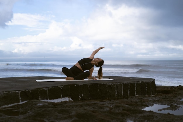 Yoga di pratica della giovane donna su una bella spiaggia all'alba. Cielo blu, oceano, onde, vicinanza alla natura, unità con la natura.