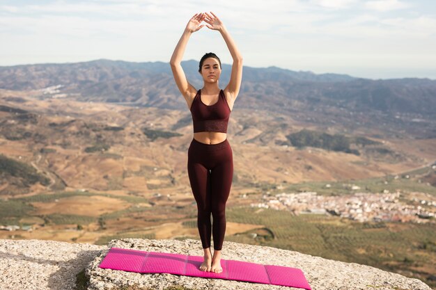 Yoga di pratica della giovane donna sulla cima della montagna