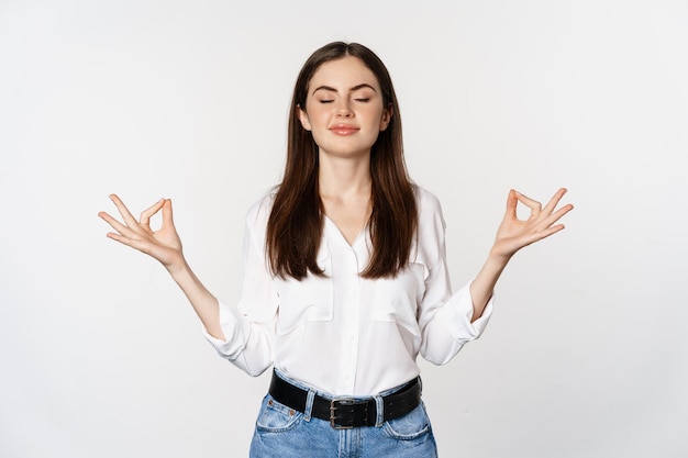 Yoga e consapevolezza. Giovane donna che medita con gli occhi chiusi, respira liberamente e mostra il segno del nirvana mudra, in piedi in pace su sfondo bianco.