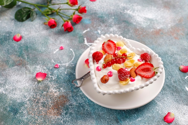 Yogurt con fiocchi di mais e frutti di bosco in una ciotola a forma di cuore.