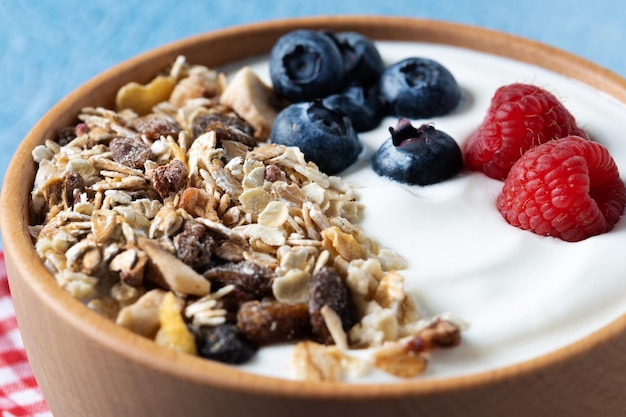 Yogurt con frutti di bosco e muesli per colazione in ciotola su sfondo lbue