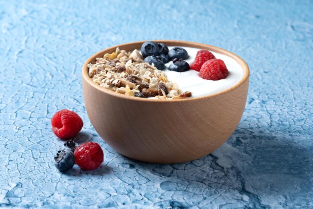 Yogurt con frutti di bosco e muesli per colazione in ciotola su sfondo lbue