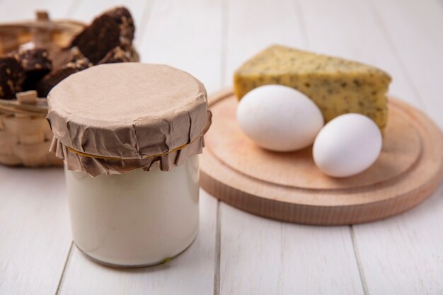 Yogurt di vista frontale in un barattolo con formaggio e uova di gallina su un supporto su uno sfondo bianco