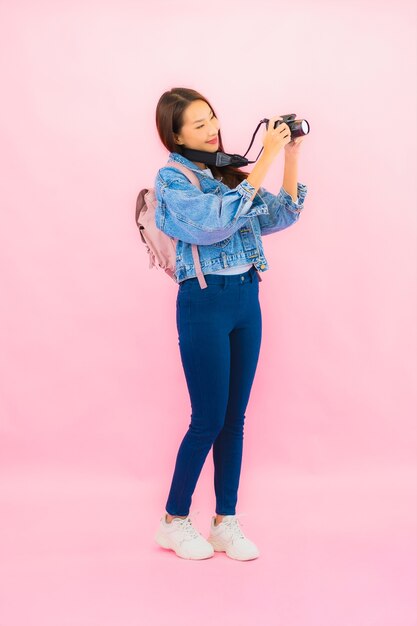 Zaino o bagaglio della bella giovane donna asiatica del ritratto con la macchina fotografica pronta per il viaggio in vacanza sulla parete rosa