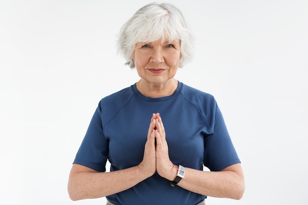 Zen, rilassamento, pensione e meditazione. adorabile energica donna di mezza età pensionato a praticare yoga, tenendo le mani unite nel gesto di namaste, facendo sequenza di saluto al sole