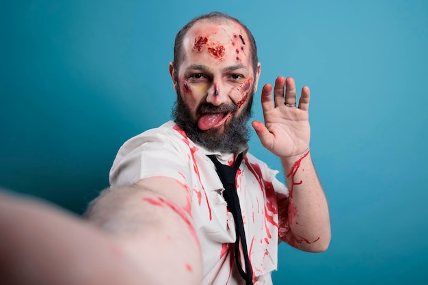 Zombie inquietante e inquietante che scatta foto sulla fotocamera, posa in studio e sembra pericoloso. Cadavere mangiatore di cervelli con cicatrici e ferite sanguinanti, mostro aggressivo horror con sguardo apocalittico.