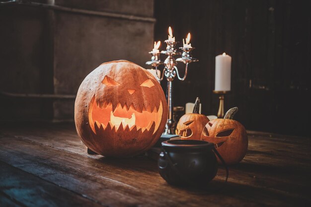 Zucche intagliate tradizionali di Halloween, piccola caldaia e candele sul pavimento di legno.