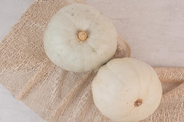 Zucche mature bianche sulla tavola bianca con tela da imballaggio.