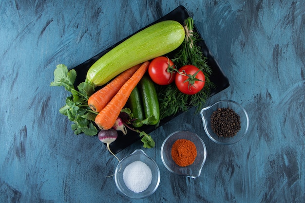 Zucchine fresche, carote, pomodori e verdure su banda nera con spezie.