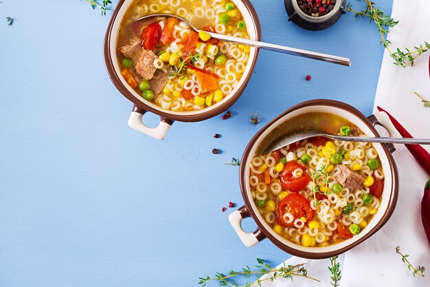 Zuppa con pasta piccola, verdure e pezzi di carne in una ciotola sul tavolo blu. Cibo italiano. Vista dall'alto. Disteso