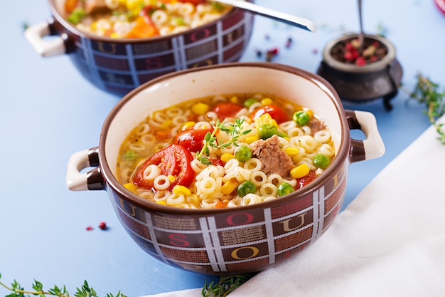 Zuppa con pasta piccola, verdure e pezzi di carne in una ciotola sul tavolo blu. Cibo italiano.