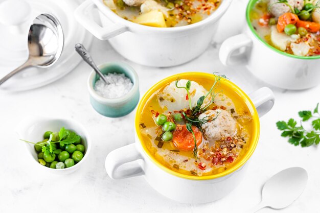 Zuppa con polpette di cavolfiore piselli carote e crema su sfondo bianco Messa a fuoco selettiva