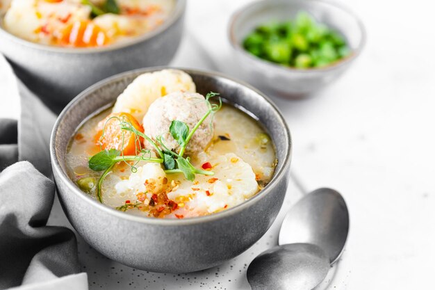 Zuppa con polpette di cavolfiore piselli carote e crema su sfondo bianco Messa a fuoco selettiva