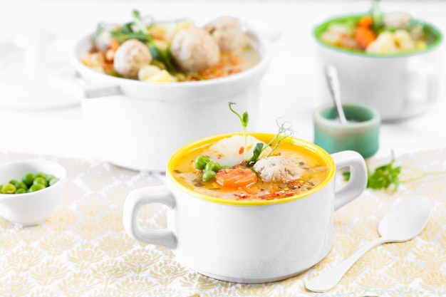Zuppa con polpette di cavolfiore piselli carote e crema su sfondo bianco