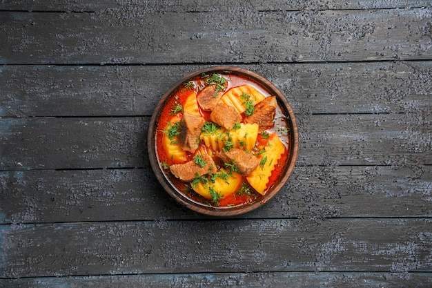 Zuppa di carne vista dall'alto con patate e verdure all'interno del piatto su una scrivania scura