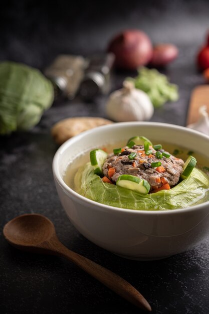 Zuppa di cavolo cappuccio di maiale con carote, cipolle verdi tritate, cetriolo in un piatto di legno su un piatto di legno