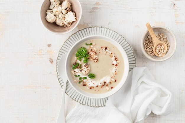 Zuppa di crema di cavolfiore con noci di pino in una ciotola su uno sfondo bianco