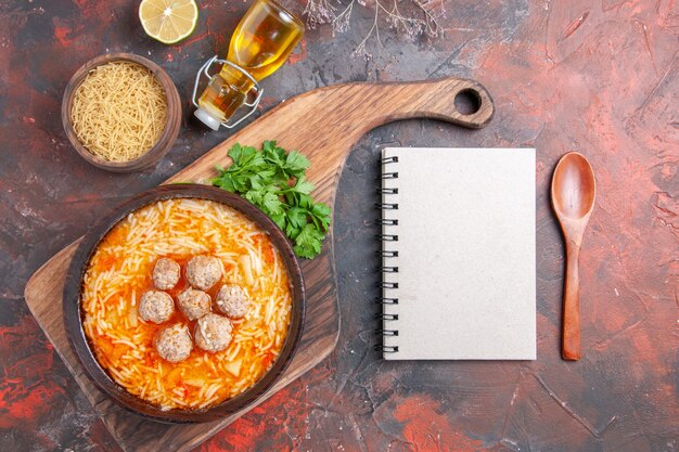 Zuppa di polpette con noodles a bordo pasta cruda verdure al limone e cucchiaio per notebook su sfondo scuro immagine stock