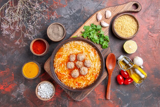 Zuppa di polpette con tagliatelle a bordo pasta cruda cime di limone bottiglia di olio cucchiaio e spezie diverse sul tavolo scuro