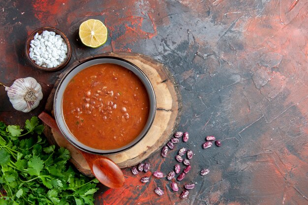 Zuppa di pomodoro in una ciotola blu cucchiaio sul vassoio di legno aglio sale e limone un mazzo di verde sul metraggio tavolo di colore misto