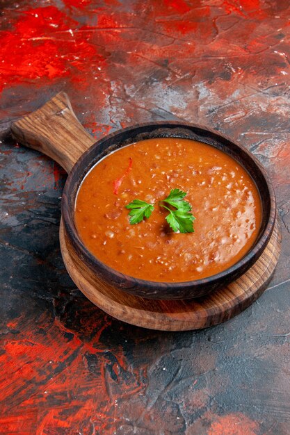 Zuppa di pomodoro verticale su un tagliere marrone sul lato destro di uno sfondo di colore misto