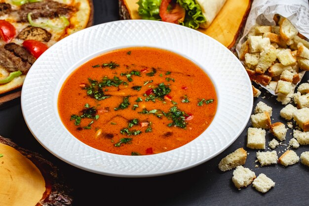 Zuppa di pomodoro vista laterale con verdure e fette biscottate di pane sul tavolo