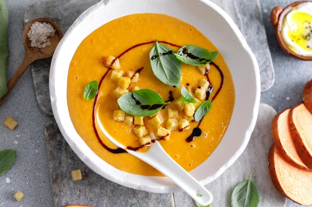 Zuppa di purè di zucca con crostini di pane e basilico servita in una ciotola sul tavolo