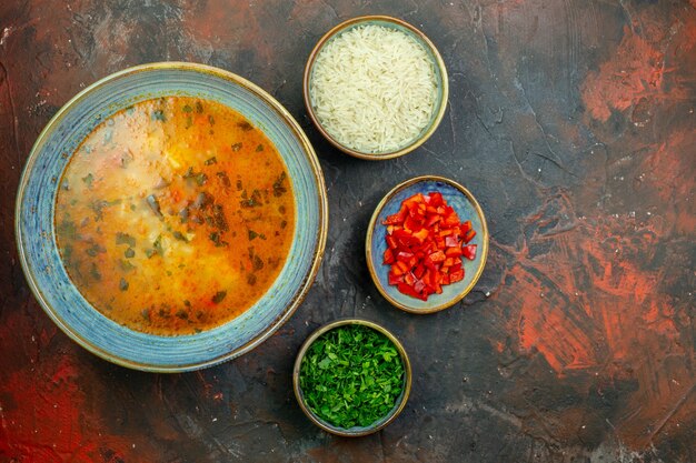 Zuppa di riso vista dall'alto in una ciotola blu peperoni tritati riso verdure tritate in ciotole sul tavolo rosso scuro