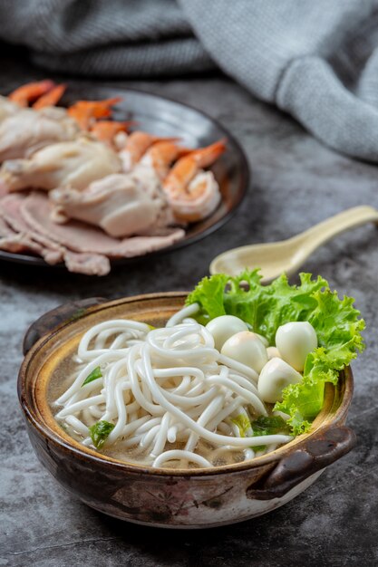 Zuppa di stile asiatico con noodles, carne di maiale e cipolle verdi da vicino in una ciotola sul tavolo.