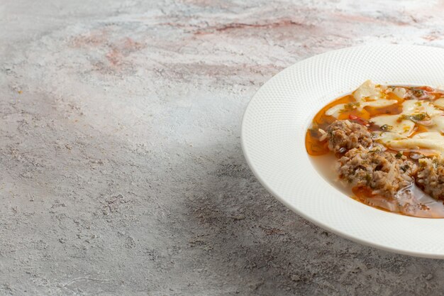Zuppa di vista ravvicinata frontale con deliziosa zuppa di carne con pasta e carne sulla superficie bianca
