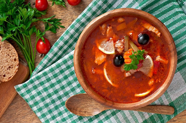 Zuppa solyanka russa con carne, olive e cetriolini in ciotola di legno