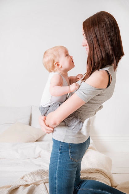 1 giovane donna bianca con i capelli castani in jeans e una camicia grigia che tiene in braccio un bambino, una madre con una figlia piccola