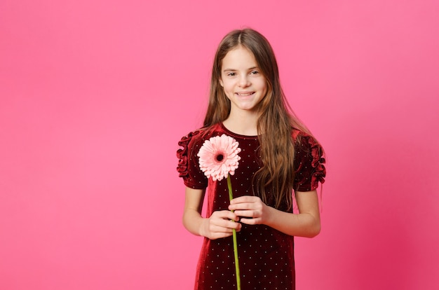1 ragazza in un vestito rosso con un fiore di gerbera su una superficie rosa
