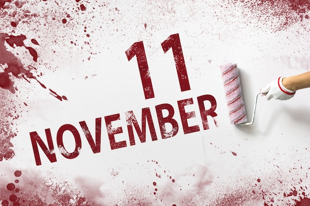 11 novembre. Giorno 11 del mese, data del calendario. La mano tiene un rullo con vernice rossa e scrive una data di calendario su uno sfondo bianco. Mese autunnale, concetto di giorno dell'anno.