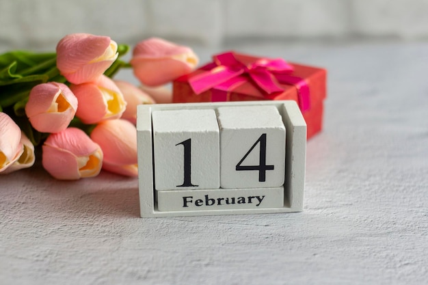 14 febbraio su un calendario in legno su sfondo grigio con tulipani rosa. San Valentino.