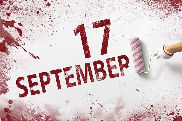 17 settembre. Giorno 17 del mese, data del calendario. La mano tiene un rullo con vernice rossa e scrive una data di calendario su uno sfondo bianco. Mese autunnale, concetto di giorno dell'anno.