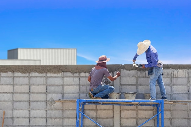 2 lavoratori edili su ponteggi stanno intonacando cemento sul bordo del muro di recinzione di blocchi di cemento