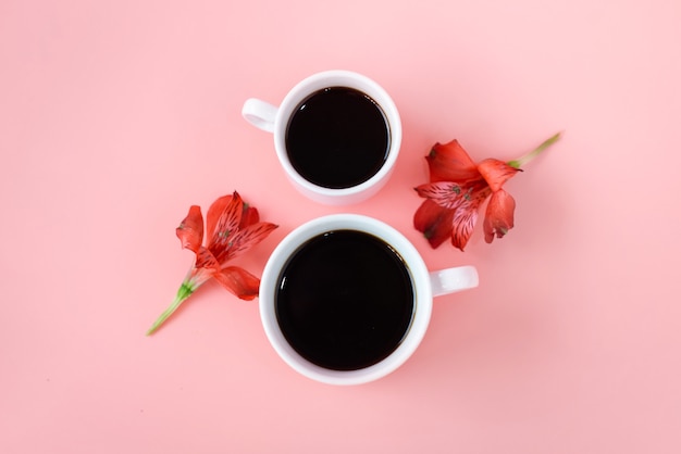 2 tazze di caffè con fiori su sfondo rosa.