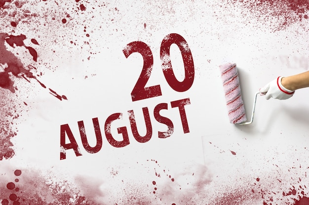 20 agosto. Giorno 20 del mese, data del calendario. La mano tiene un rullo con vernice rossa e scrive una data di calendario su uno sfondo bianco. Mese estivo, concetto di giorno dell'anno.