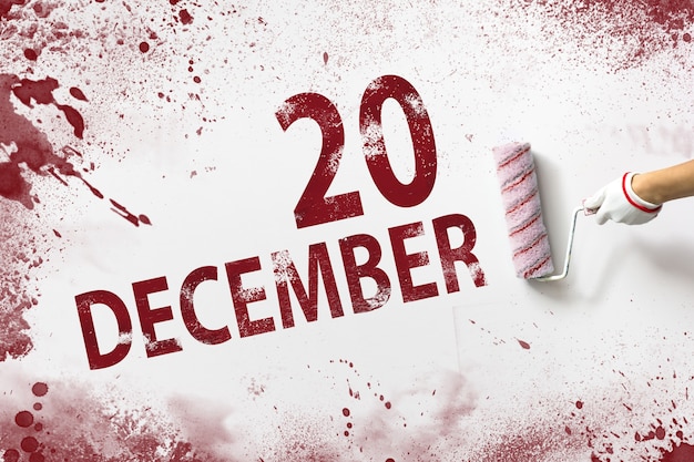 20 dicembre. Giorno 20 del mese, data del calendario. La mano tiene un rullo con vernice rossa e scrive una data di calendario su uno sfondo bianco. Mese invernale, concetto di giorno dell'anno.