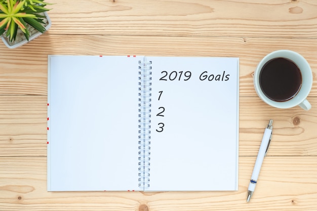 2019 Obiettivi con notebook, tazza di caffè nero, penna e bicchieri sul tavolo