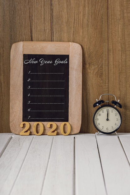 2020 testo in legno e lista degli obiettivi di Capodanno scritti sulla lavagna con sveglia