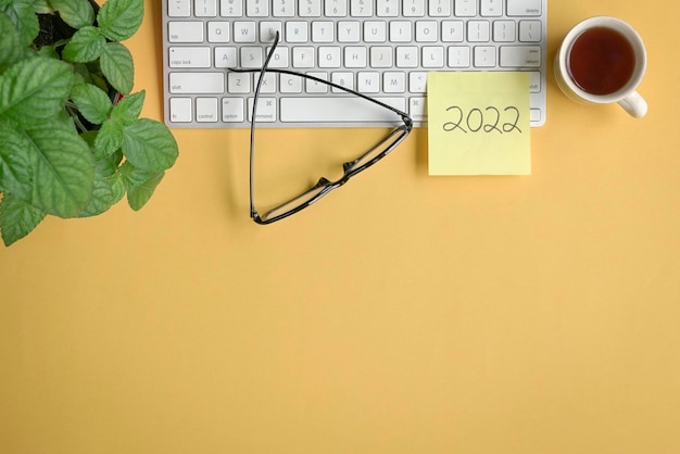 2022 scritto su un bastoncino di carta giallo sopra la tastiera con occhiali da caffè e pianta