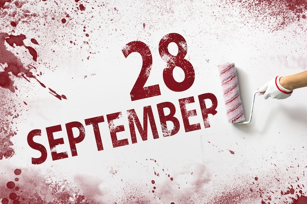 28 settembre. Giorno 28 del mese, data del calendario. La mano tiene un rullo con vernice rossa e scrive una data di calendario su uno sfondo bianco. Mese autunnale, concetto di giorno dell'anno.