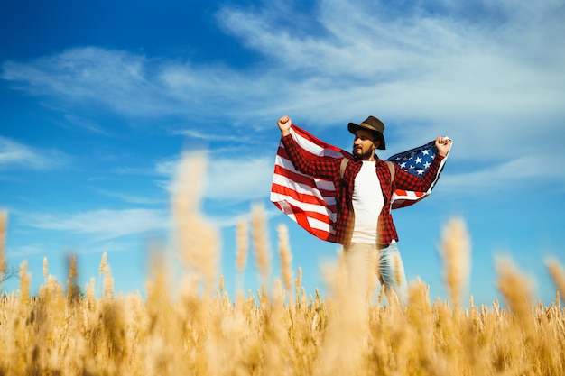 4 luglio. Quattro luglio. Americano con la bandiera nazionale. Bandiera americana. Giorno dell'Indipendenza. Vacanze patriottiche. L'uomo indossa un cappello, uno zaino, una camicia e jeans.