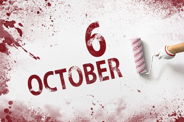 6 ottobre. Giorno 6 del mese, data del calendario. La mano tiene un rullo con vernice rossa e scrive una data di calendario su uno sfondo bianco. Mese autunnale, concetto di giorno dell'anno.